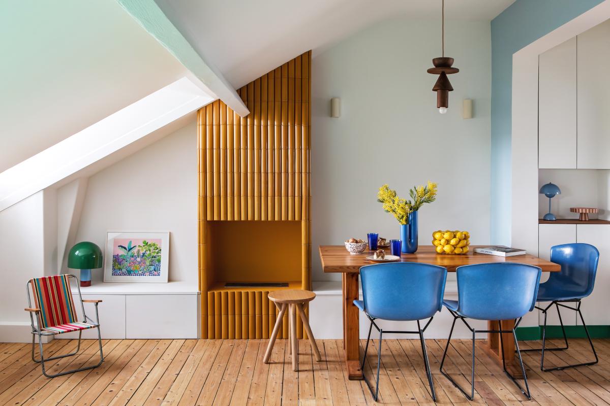Salon avec cheminée habillée de faïence, table et chaises colorées.